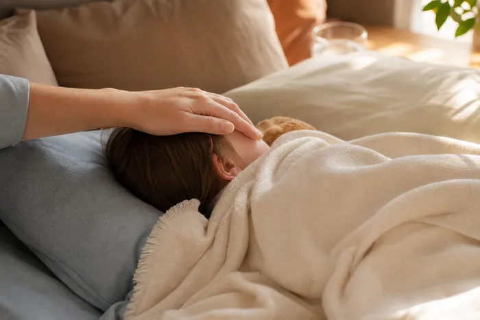 A parent’s hand resting on a sleeping child’s forehead to check for fever