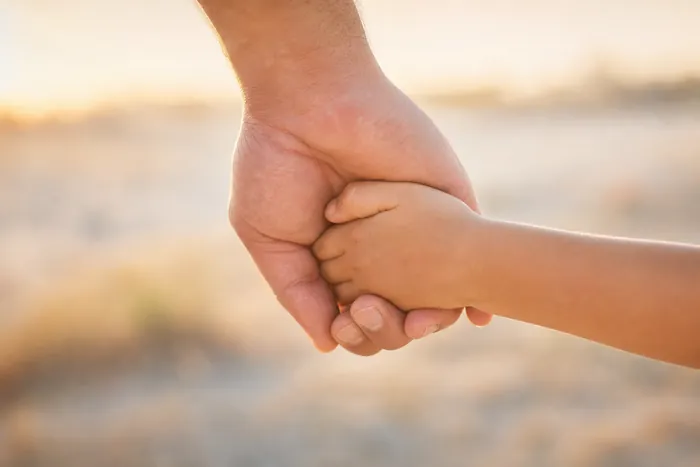 An adult hand holding a small child’s hand in warm evening light