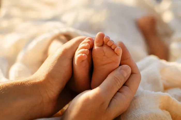 An adult’s hands cradling a newborn baby’s feet on a soft blanket