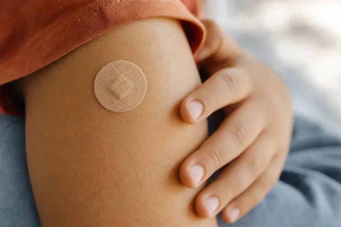 A small round bandage on a young child’s upper arm after a vaccination